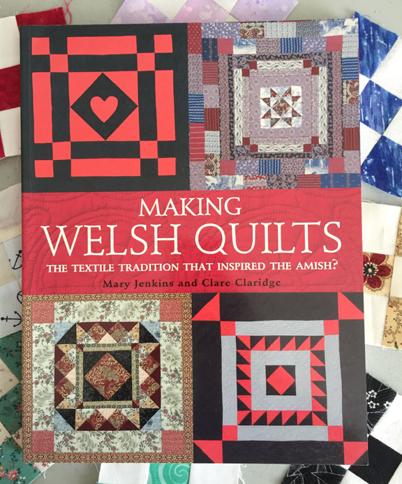 Image of the cover of Mary Jenkins and Clare Claridge's book, titled Making Welsh Quilts: The Textile Tradition that Inspired the Amish? The book rests on a background of small nine-patch quilt blocks.