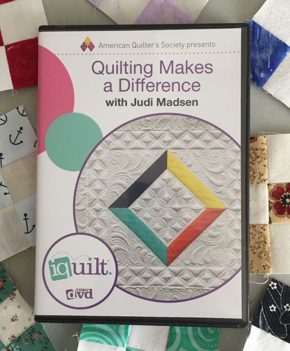 Image of the cover of a DVD called Quilting Makes a Difference with Judi Madsen. The DVD rests on a background of small nine-patch quilt blocks.